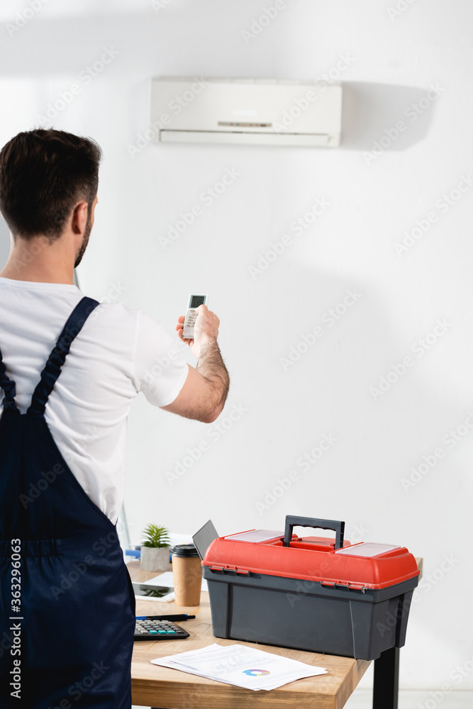 back view of repairman near toolbox holding air conditioner remote controller back view of repairman near toolbox holding air conditioner remote controller