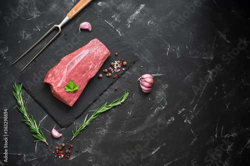 Raw beef filet with rosemary and spices on a black stone background. Top view, flat lay, copy space.