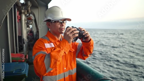 Filipino deck Officer on deck of vessel or ship , wearing PPE personal protective equipment. He is looking through binoculars. photo