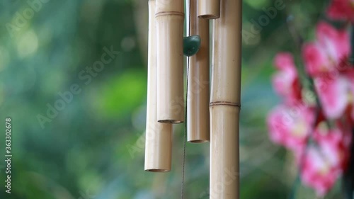 Sinos de vento feitos de bambu se mexendo em um a brisa num jardim com flores ao fundo photo