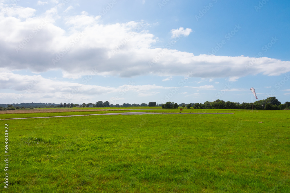 Beautiful long shot of a field used as a takeoff/landing runway for planes. Small airdrome in the countryside. Sunny day with no wind as the windsock indicates. Beautiful long shot of a field used as a takeoff/landing runway for planes. Small airdrome in the countryside. Sunny day with no wind as the windsock indicates.