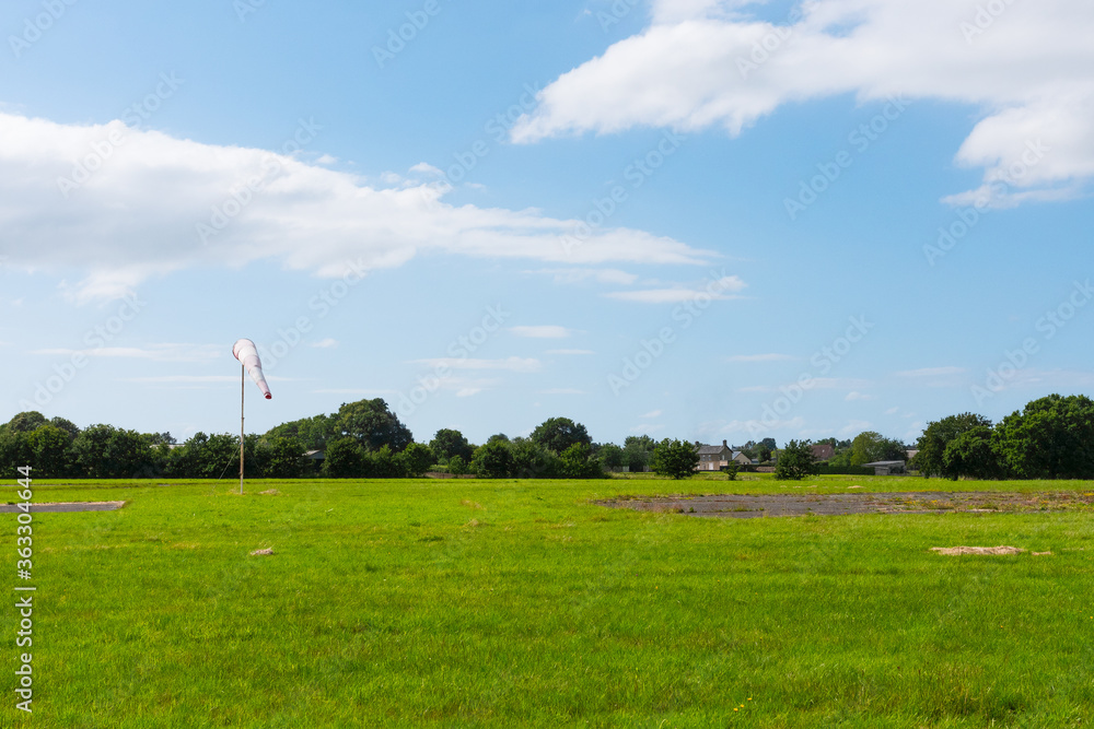 Beautiful long shot of a field used as a takeoff/landing runway for planes. Small airdrome in the countryside. Sunny day with no wind (windsock instrument). Beautiful long shot of a field used as a takeoff/landing runway for planes. Small airdrome in the countryside. Sunny day with no wind (windsock instrument).