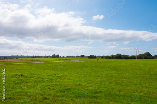 Beautiful long shot of a field used as a takeoff landing runway for planes. Small airdrome in the countryside. Sunny day with no wind as the windsock indicates. 