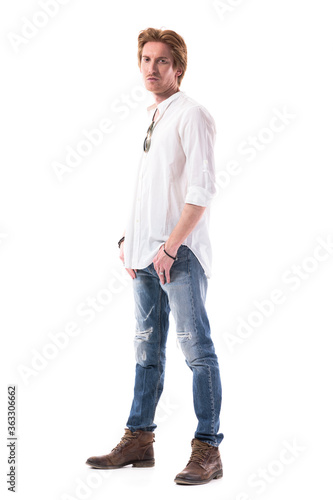 Confident handsome stylish redhead man in jeans looking at camera with hands in pockets. Full body length isolated on white background. 