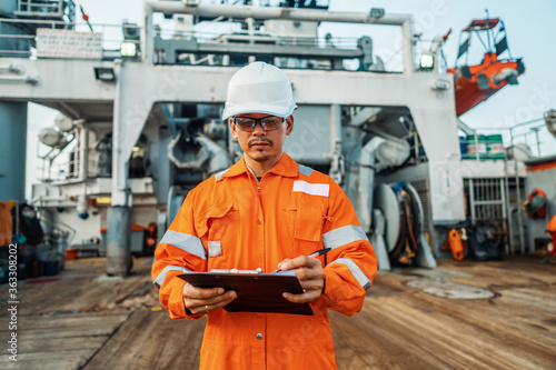 Filipino deck Officer on deck of offshore vessel or ship , wearing PPE personal protective equipment. He fills checklist. Paperwork at sea photo