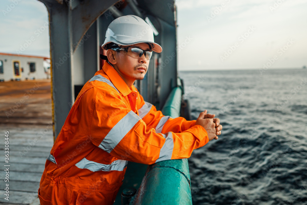 Filipino deck Officer on deck of vessel or ship , wearing PPE personal protective equipment - helmet, coverall, lifejacket, goggles. Safety at sea. He is tired Filipino deck Officer on deck of vessel or ship , wearing PPE personal protective equipment - helmet, coverall, lifejacket, goggles. Safety at sea. He is tired
