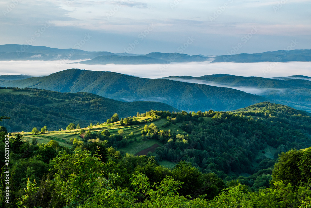 green meadow on which the sun shines against the background of mountain peaks in the fog. morning in the mountains.