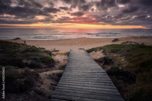 Fototapeta Naklejka Na Ścianę i Meble -  Camino de madera hasta la playa con puesta de sol al fondo