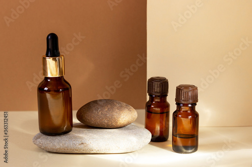 Glass cosmetic bottles with a dropper stand next to a log on a beige background with bright sunlight. The concept of natural cosmetics, natural essential oil.