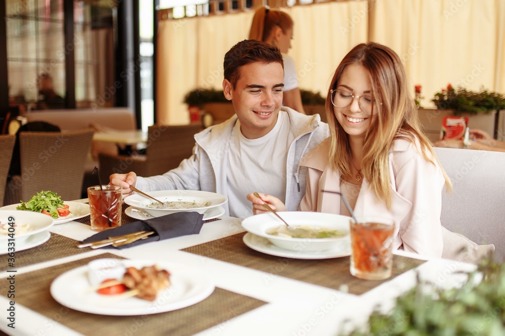 A cheerful and beautiful couple are relaxing on a summer terrace in a restaurant with food and drinks. The guy and the girl have fun on the terrace A cheerful and beautiful couple are relaxing on a summer terrace in a restaurant with food and drinks. The guy and the girl have fun on the terrace