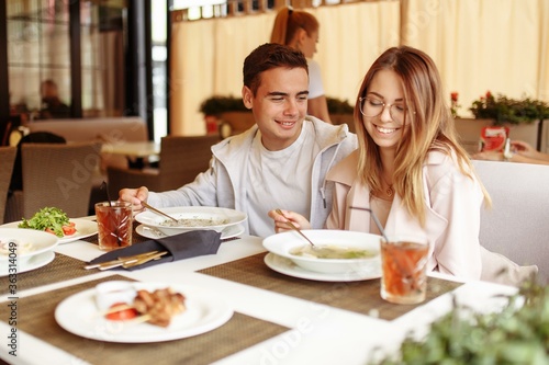 A cheerful and beautiful couple are relaxing on a summer terrace in a restaurant with food and drinks. The guy and the girl have fun on the terrace