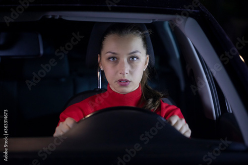Woman is driving car at night. Serious female driver sitting inside car looks confused forward to the road clings tight to wheel on night trip. Concept: nerves and transportation. Safe journey