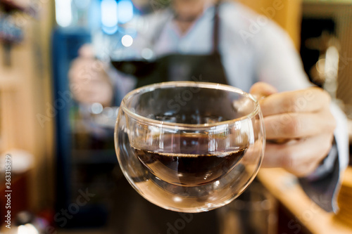 Double glass cup close-up with coffee in cafe. Barista gives a cup of coffee to you. Alternative coffee brewing using Syphon device.