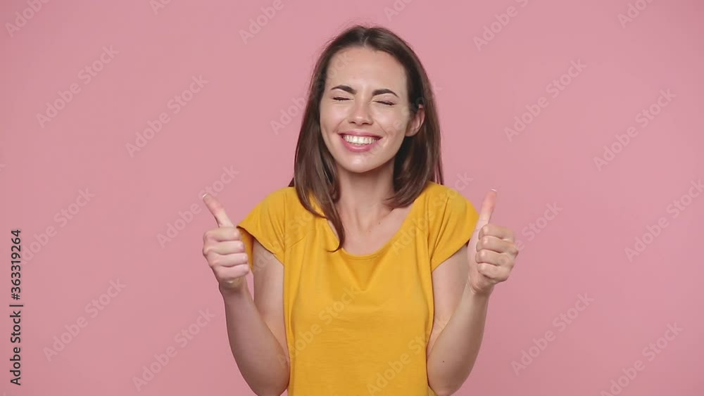 Smiling happy beautiful brunette young woman 20s years old in yellow t-shirt posing isolated on pastel pink background studio. People lifestyle concept. Looking camera showing thumbs up hands gesture Smiling happy beautiful brunette young woman 20s years old in yellow t-shirt posing isolated on pastel pink background studio. People lifestyle concept. Looking camera showing thumbs up hands gesture