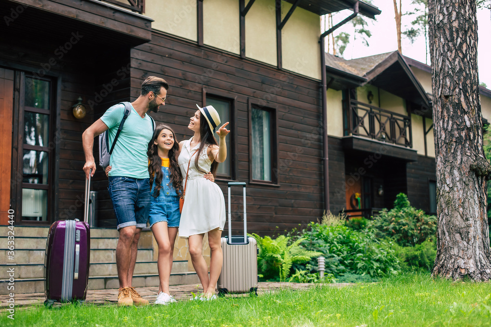 Photo of a beautiful young tourist family on vacation while them standing on forest hotel background and waiting to get settled in the room with backpacks and suitcases. Photo of a beautiful young tourist family on vacation while them standing on forest hotel background and waiting to get settled in the room with backpacks and suitcases.