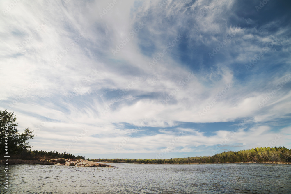 Wide shot of dramatic prairie sky over blue lake surrounded by trees and Canadian shield Wide shot of dramatic prairie sky over blue lake surrounded by trees and Canadian shield