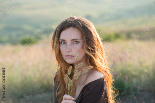 beautiful young girl walks in a summer field at sunset