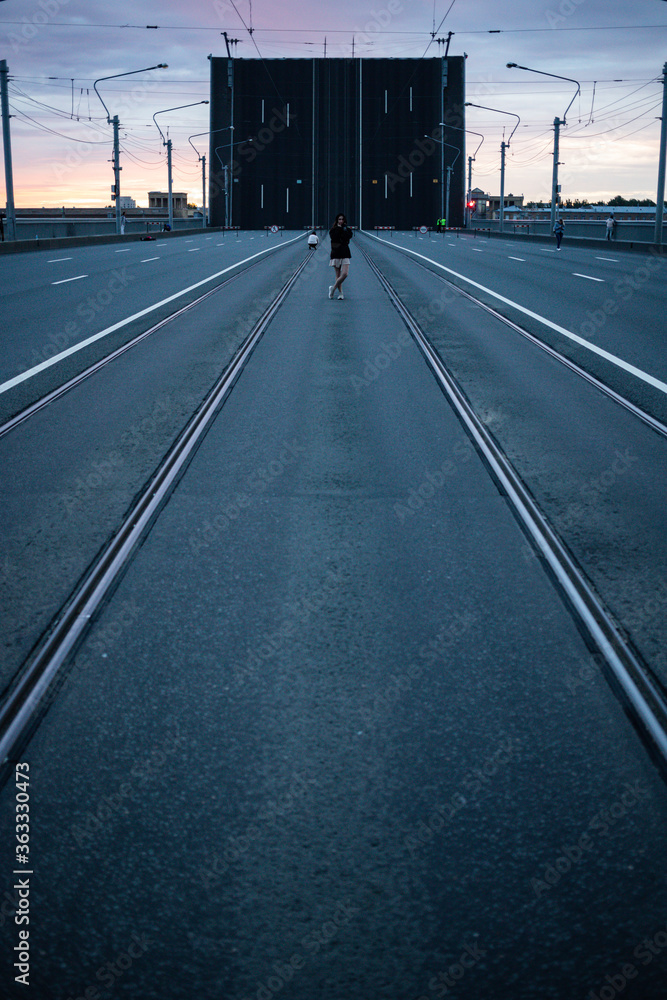a road with rails stretching away into the horizon and a girl standing in the middle of a beautiful sunrise against the backdrop of a drawbridge a road with rails stretching away into the horizon and a girl standing in the middle of a beautiful sunrise against the backdrop of a drawbridge