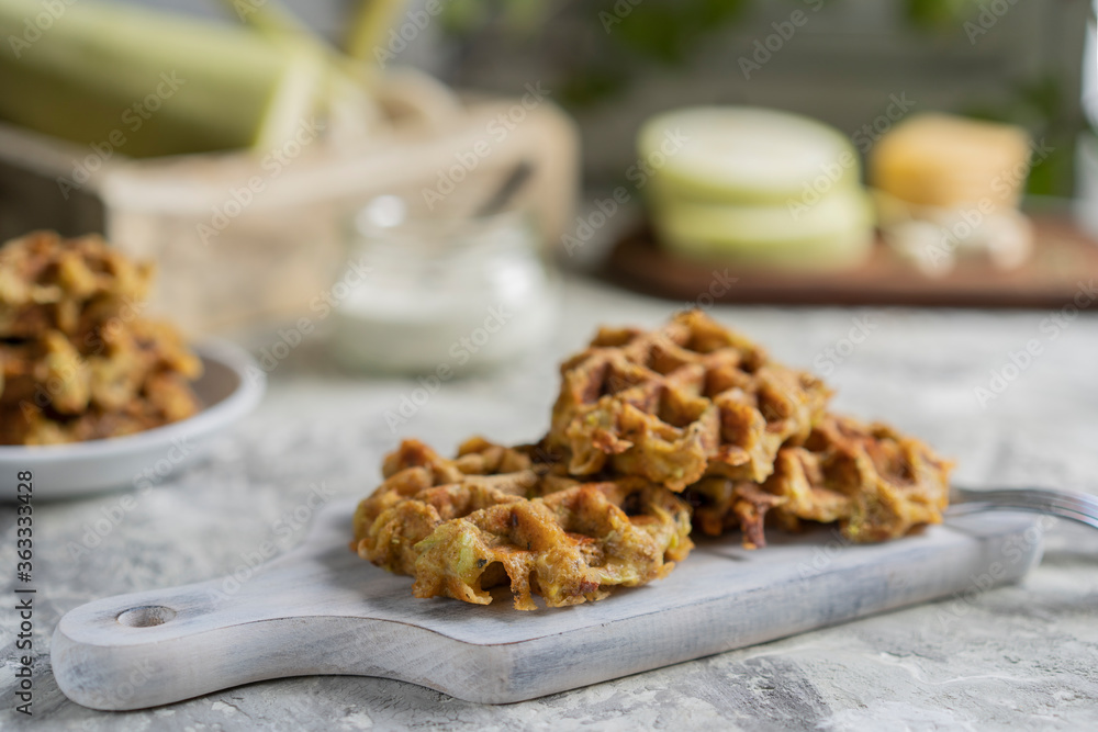 Savory squash or zucchi waffles with cheese, herbs and white sauce. Homemade baked waffles on grey textured table at kitchen, natural light, organic products on background. Selective focus, copy space Savory squash or zucchi waffles with cheese, herbs and white sauce. Homemade baked waffles on grey textured table at kitchen, natural light, organic products on background. Selective focus, copy space