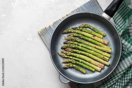 The process of making asparagus in a frying pan. Fresh asparagus in a frying pan on a grey concrete background.