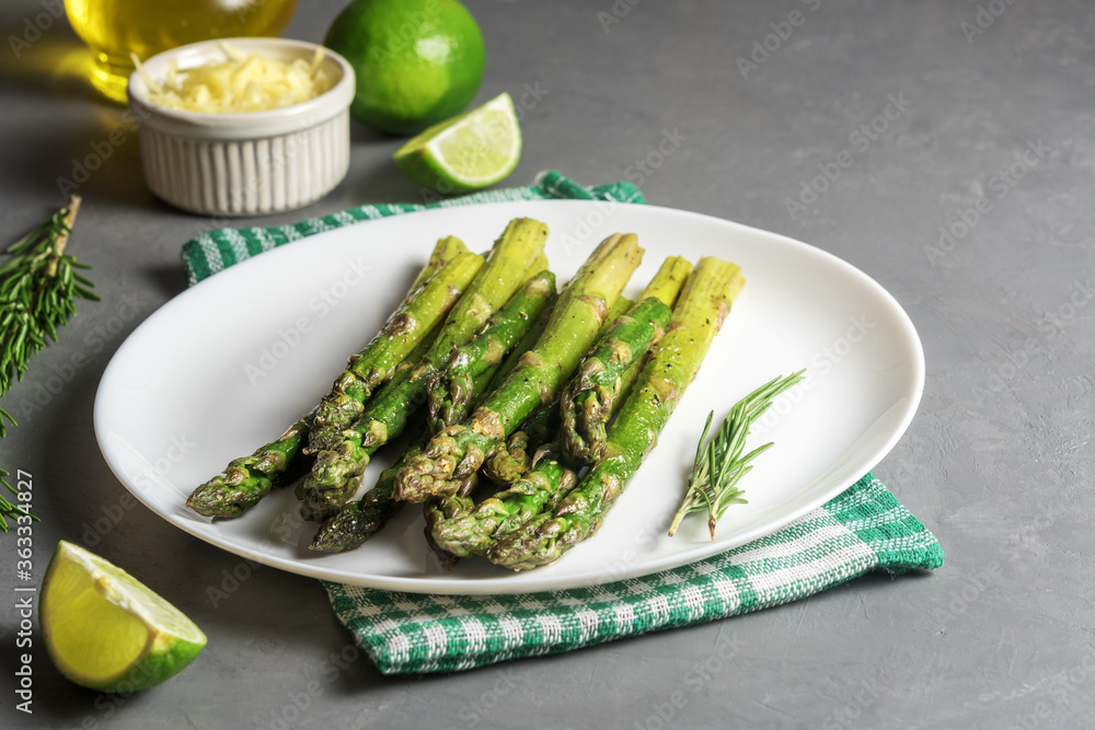 Appetizingly cooked asparagus with pieces of lime on a grey concrete table.
