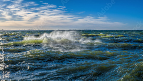 Stormy breaking sea wave with wind spray at sunny day.
