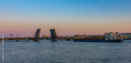 General cargo ship with raw wood logs on deck underway on Neva river at summer sunrise.