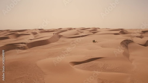 Aerial drone shot sweeping over perfect Sahara desert sand dunes as two people walk along the top of one of the dunes photo