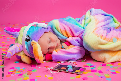 Fotografie Happy little blonde girl in unicorn kigurumi listens to music holding in hand sm