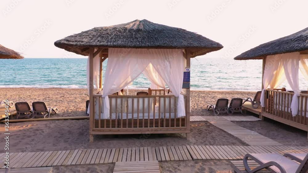 VIP area on the beach. Romantic luxury beach canopy on the beach. Aerial view sandy beach with sea waves at sunset time.