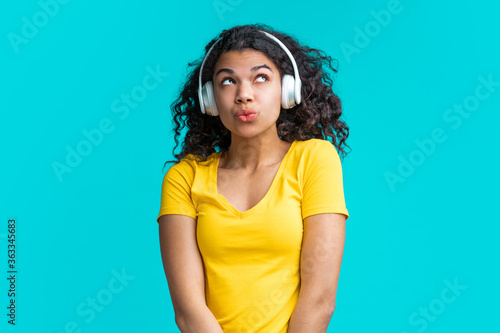 Smiling cute dark skinned girl in wireless earphones listening to music and whistling the tune