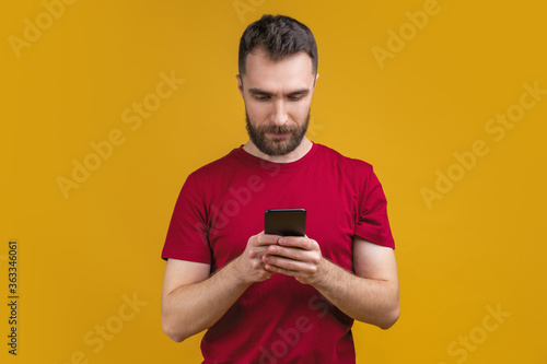 Portrait of attractive bearded man reading message on his mobile phone isolated over yellow background © wpadington