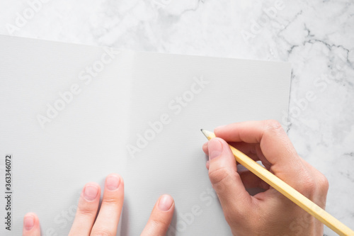 woman signs gray greeting card on marble table background. girl about to write a letter or note on a blank sheet of gray paper