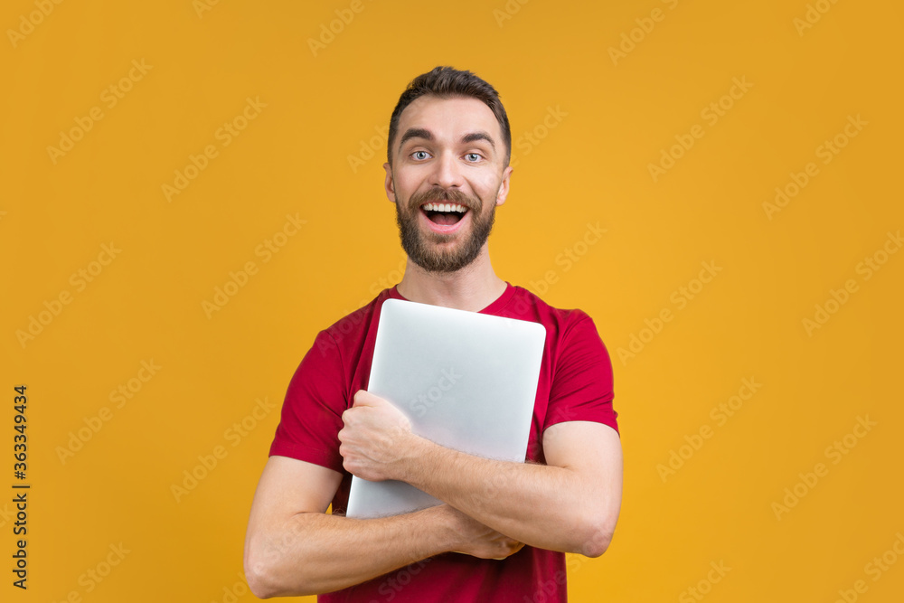 Portrait of smiling casually dressed bearded man holding laptop computer in hands isolated over bright colored background Portrait of smiling casually dressed bearded man holding laptop computer in hands isolated over bright colored background