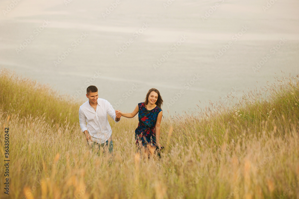 Happy couple holding hands is walking through a high grass field on a cloudy day