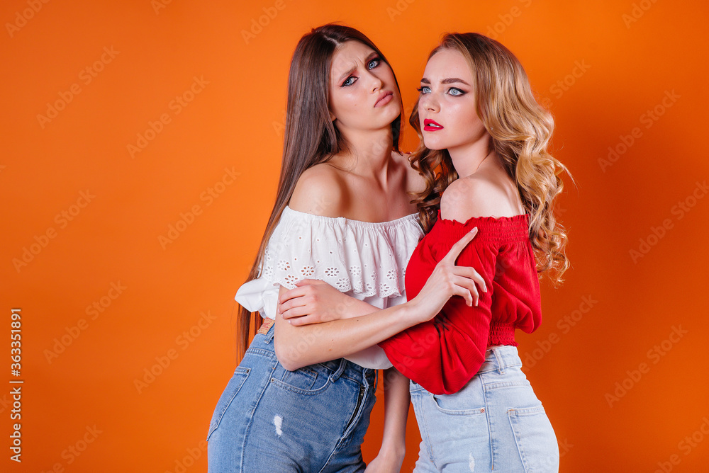 Two young and beautiful girls shows emotions and smiles in the Studio on an orange background. Girls for advertising Two young and beautiful girls shows emotions and smiles in the Studio on an orange background. Girls for advertising