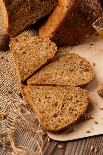 Bread in form of triangle and with nuts and honey near spikelets of wheat lies on old weathered wooden table. Rustic bread and wheat on an old vintage planked wood table. Free text space.