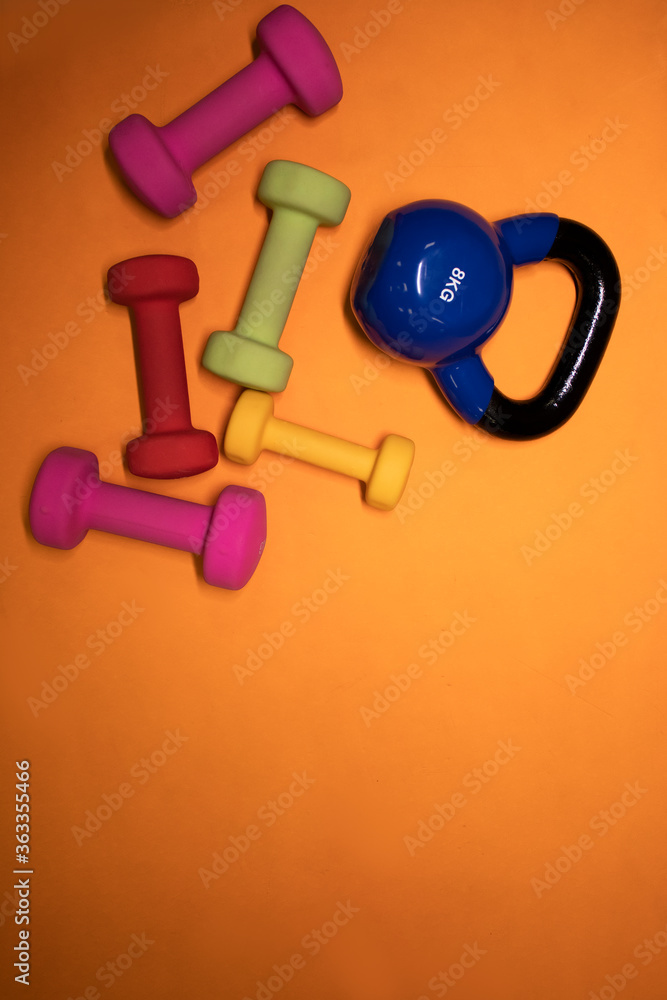 Bright pink, green, red and yellow small dumbbells and a blue kettlebell on an orange background. Sport concept. High quality photo Bright pink, green, red and yellow small dumbbells and a blue kettlebell on an orange background. Sport concept. High quality photo