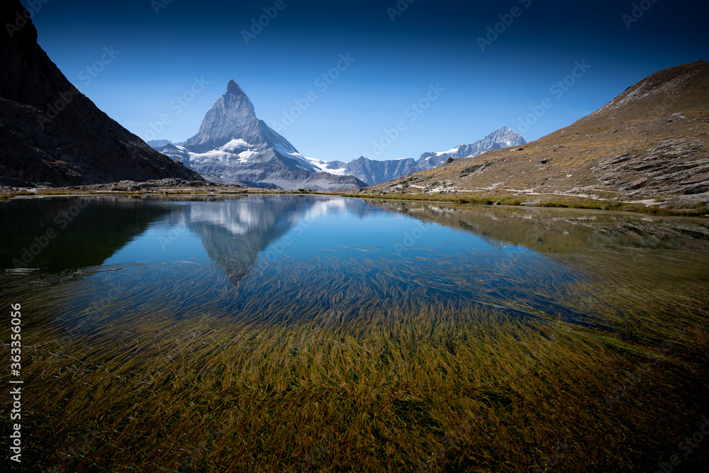 Matterhorn reflection across alpine lake by hiking trails on sunny day