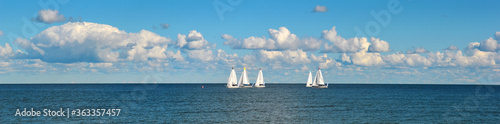 A group of sailboats or yachts, a race on a sea or ocean. Beautiful sky with clouds.