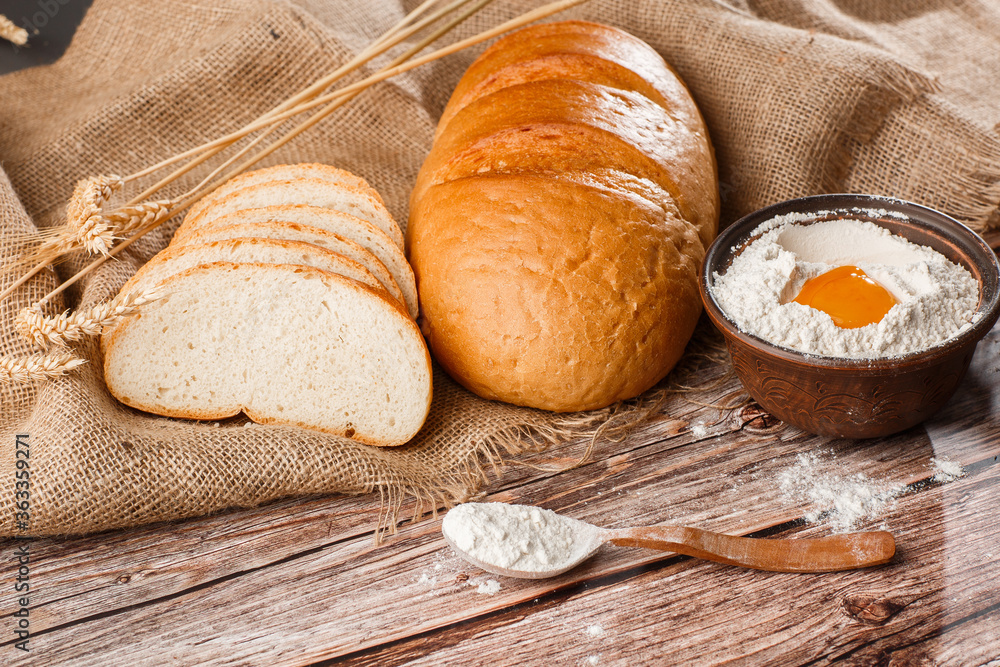 Close-up of homemade bread. Peasant loaf bread and wheat spikelets with space for text. Homemade baking. White bread with flour and egg yolk on wooden chopping board wheat rye ears copy space.