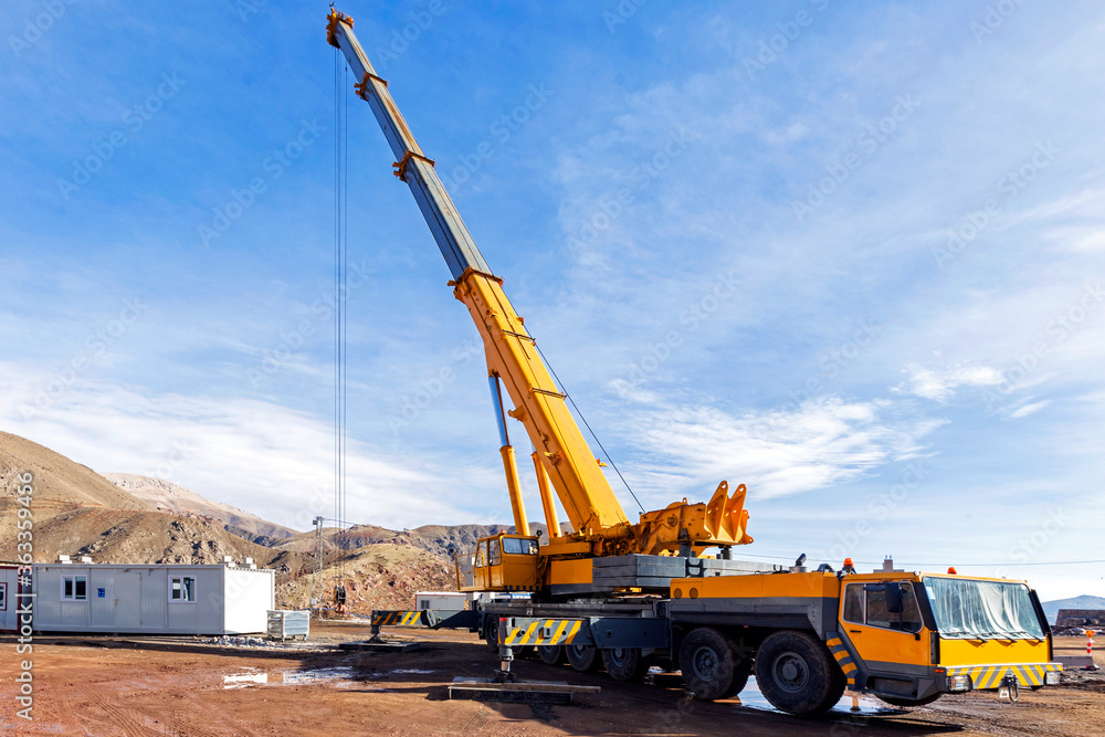 A truck-mounted crane in the construction site. The cranes have two parts. The carrier often referred to as the lower and the lifting component which includes the boom referred to as the upper.