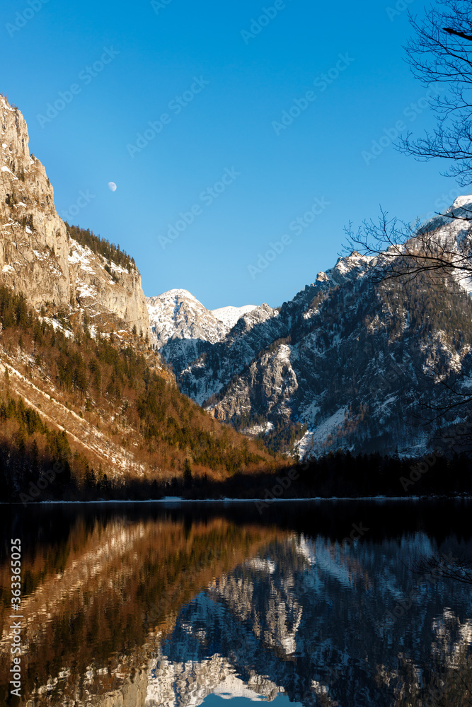 beautiful view of mountains with reflection in a alpine lake and moon in blue sky in earley spring