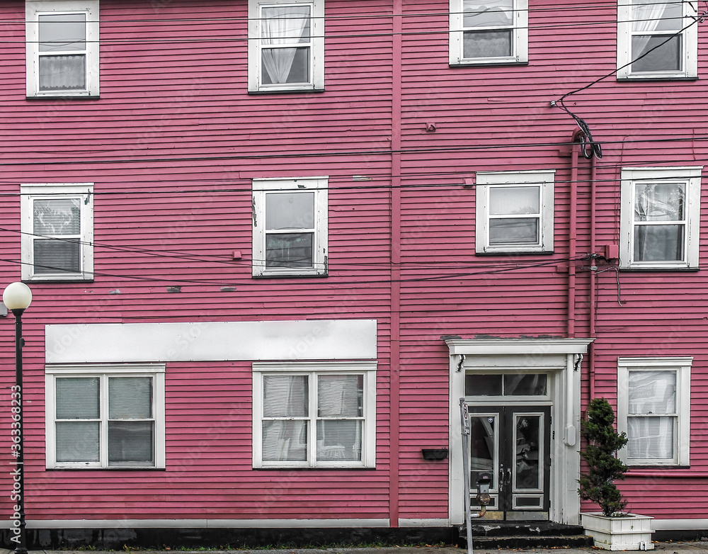 Run down rooming house exterior street view with peeling magenta siding and white door and window frames nobody