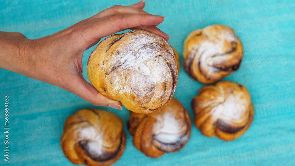 Top view of womens hand holding a sweet bun over the blurred background with other buns. Bakery concept. Space for text. Top view of womens hand holding a sweet bun over the blurred background with other buns. Bakery concept. Space for text.