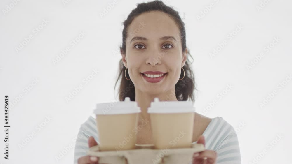 Smiling young attractive female dressed in white clothes offering to viewer two cardboard drinking cup looking at camera. 4K footage. Smiling young attractive female dressed in white clothes offering to viewer two cardboard drinking cup looking at camera. 4K footage.