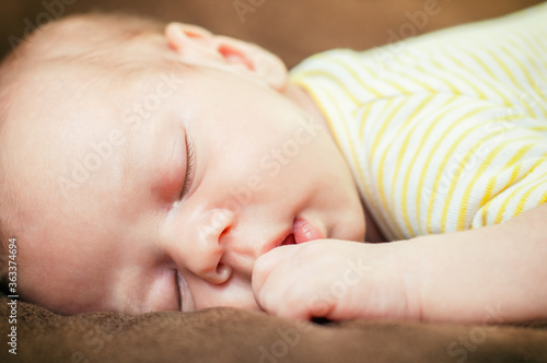 Beautiful newborn baby boy sleeping peacefully on the soft brown blanket