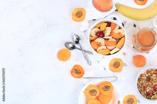 Useful breakfast with ingredients, flat lay, fruit salad with granola, apricots, bananas, honey and peaches on a bright table. The concept of a healthy and natural diet, lifestyle, top view