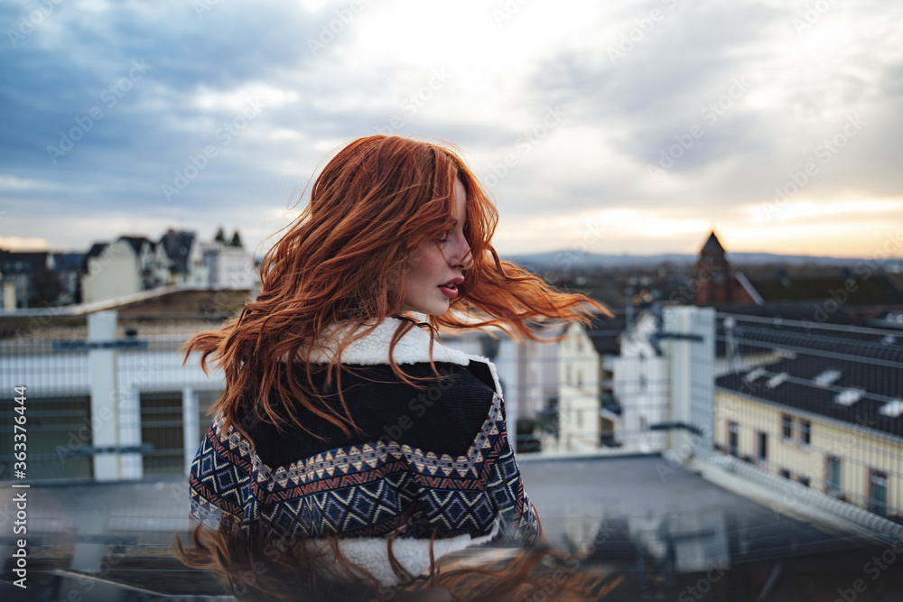 Side view of beautiful young red haired woman in evening light. Nice long wavy red hairs fluttering in wind.