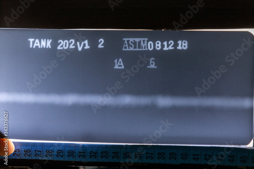 View of the industrial radiography of the weld metal with porosities defect and base metal on the light box. Tank no (202), weld no (V1, 2) and date is a figment. ASTM 1A and 6 is a penetrameter tool. photo